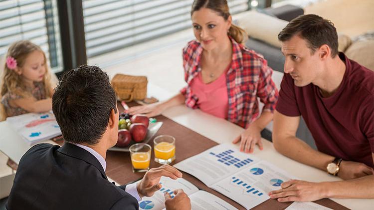 Couple discussing whether to pay for college or save for retirement with financial advisor, while daughter colors at the table.